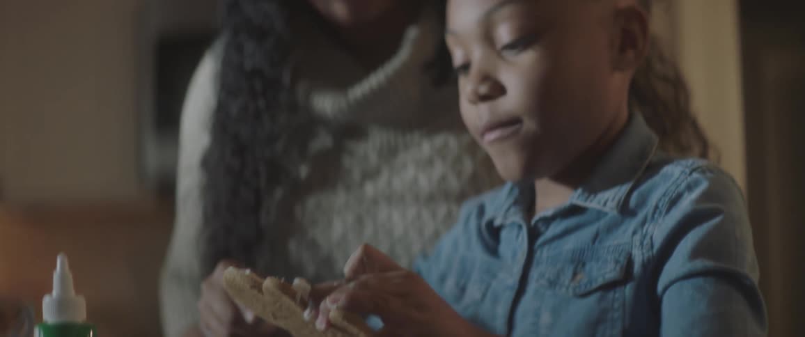 A young girl frosts a cookie as a woman watches her