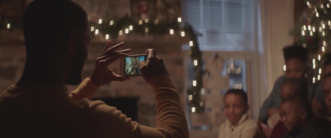 Father taking a picture of his kids in front of christmas tree on his cell phone