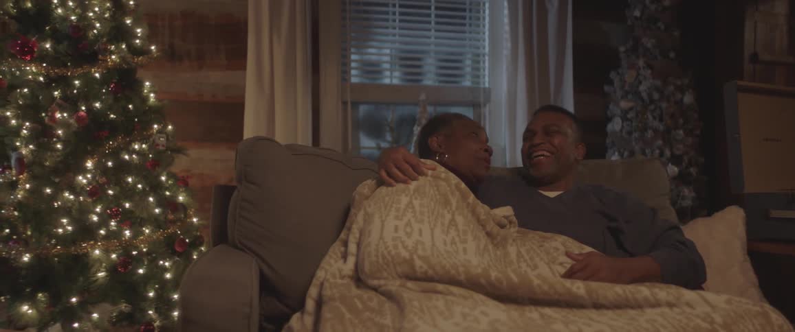 A man and woman laugh and cuddle on a couch