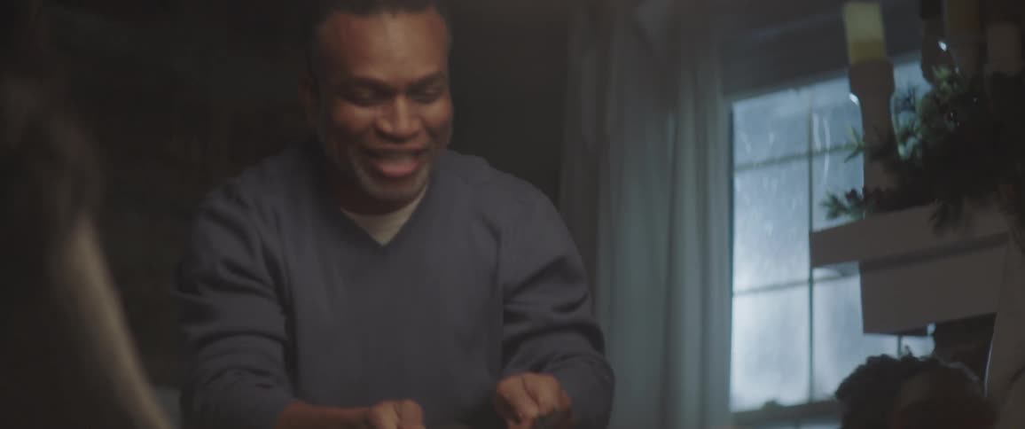 A man talking and smiling while cutting a turkey on a dining table surrounded by family