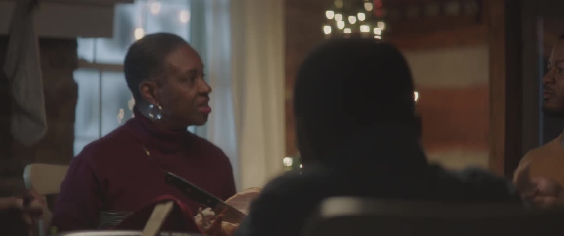 A family talks while sitting around a holiday dinner table with a christmas tree in the back