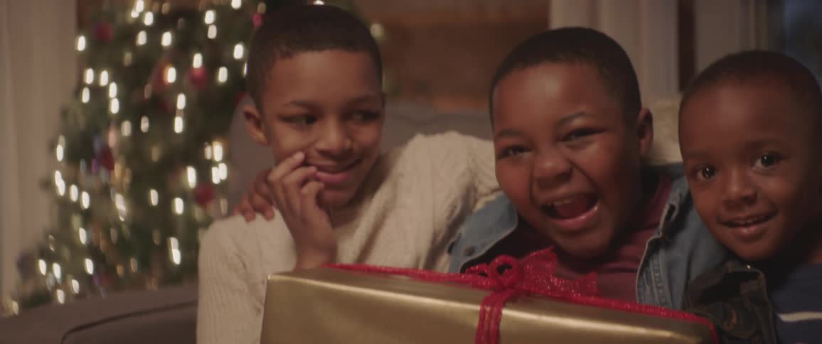 Three young boys smile as they hold a christmas present on their laps