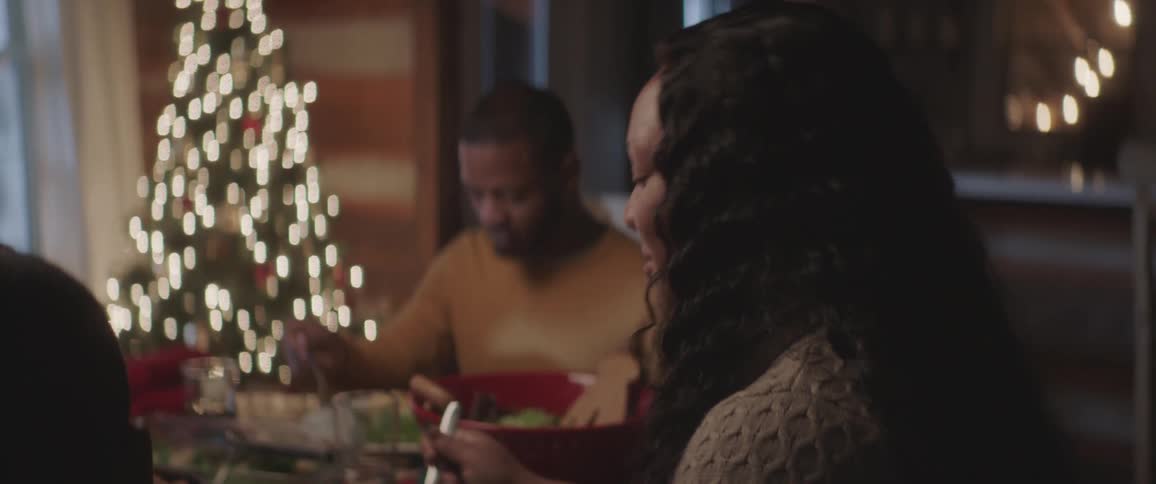 Black family sitting at the table has a christmas dinner by decorated tree at home