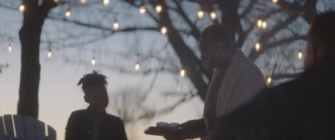 A woman showing a tray with small cups on it to a pair of children standing near a bonfire
