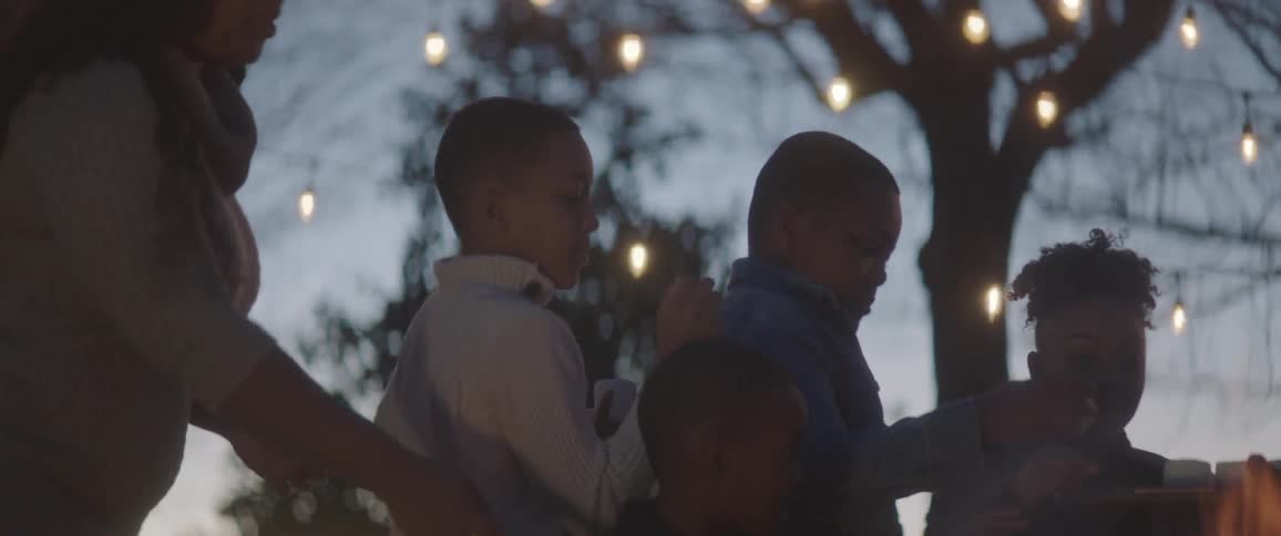 Children taking food off a serving tray while a campfire burns in the foreground