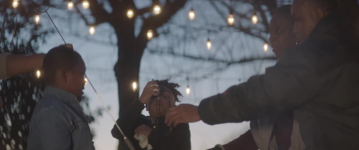 A woman hands out skewers to a family around a fire outside at night