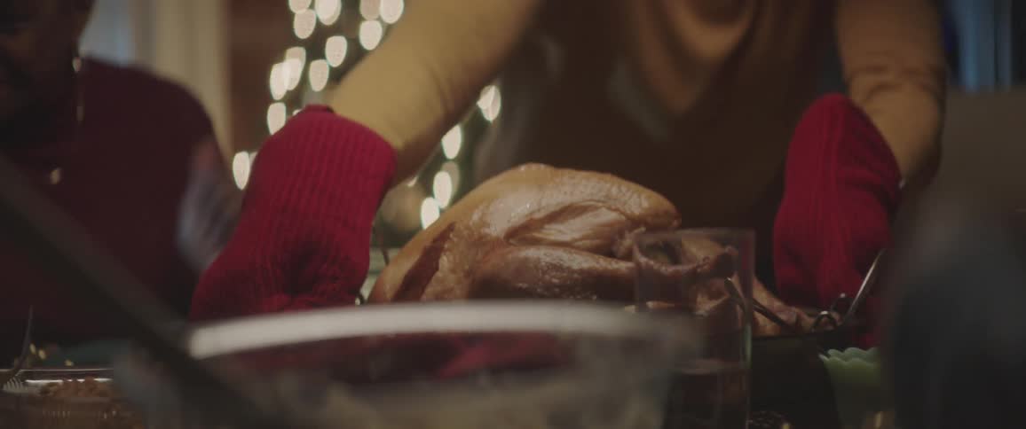 Family sits at the table and black man brings turkey to the table to celebrate christmas at night