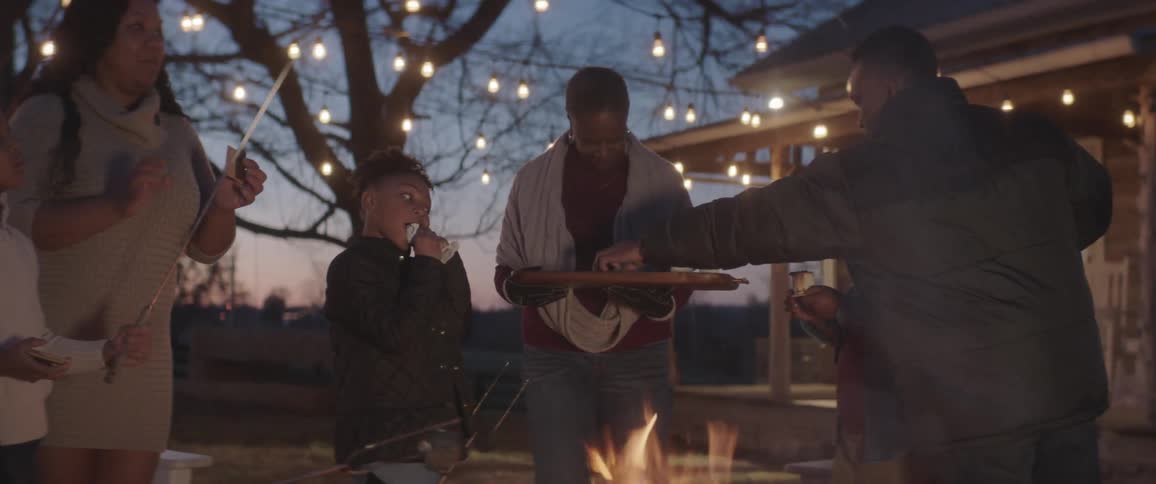Family making smores on fire pit in backyard under lights