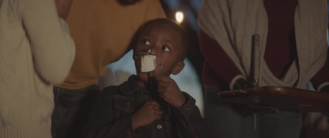 A child eats a roasted marshmallow in the yard with family