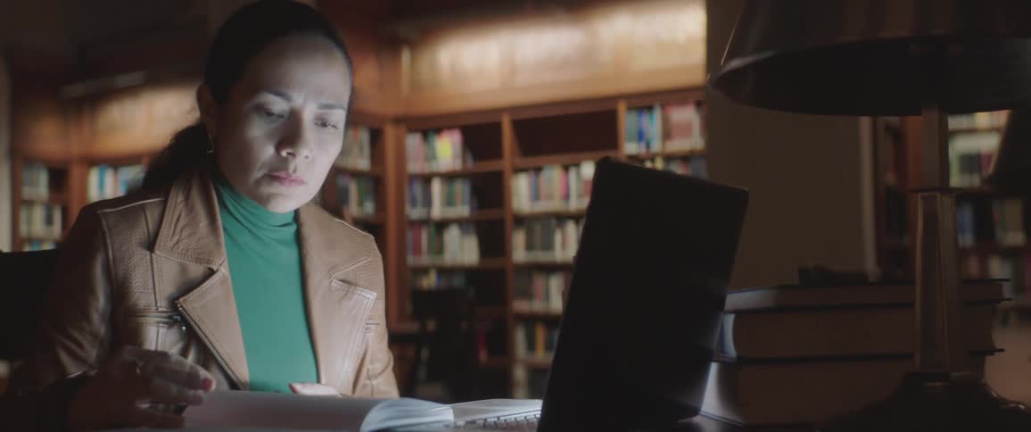 A woman thumbs through her notebook with her laptop sitting nearby