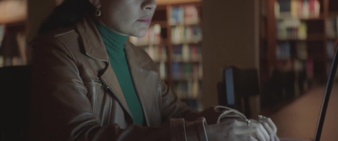 Female sitting at a table in the library typing fast on a laptop