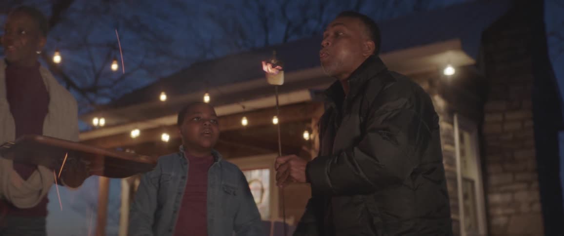 A man and a boy taking marshmallows out of the fire and blowing it