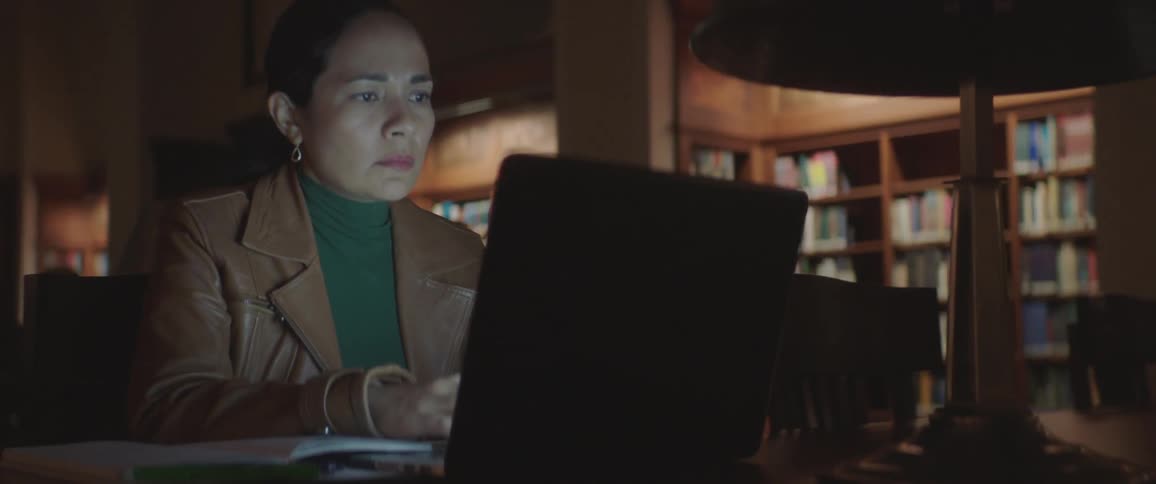 A woman works at a laptop in a dark library