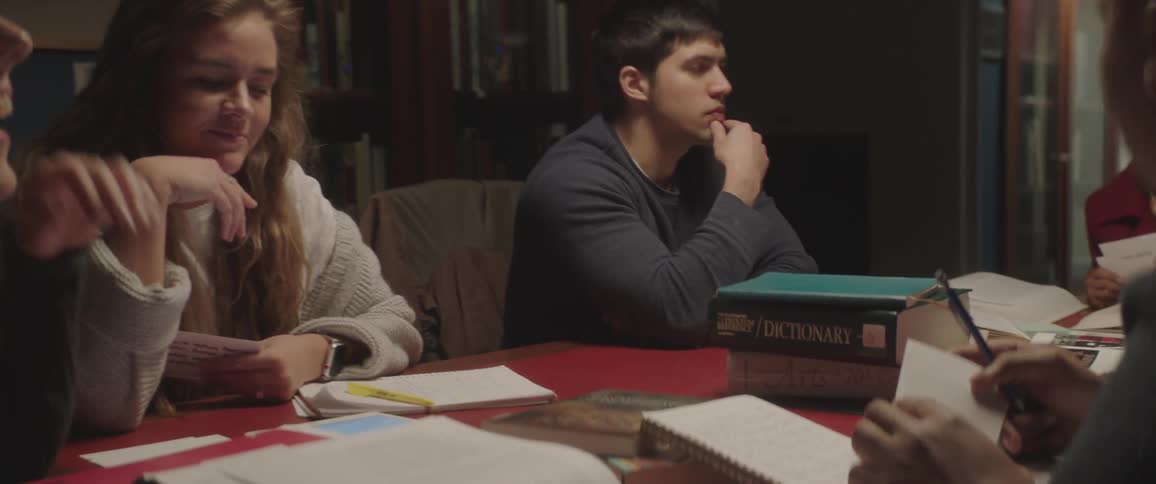 A group of teenagers study and take notes at a table in a library