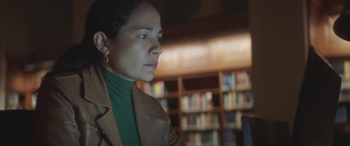 A woman types on a laptop in a dark library