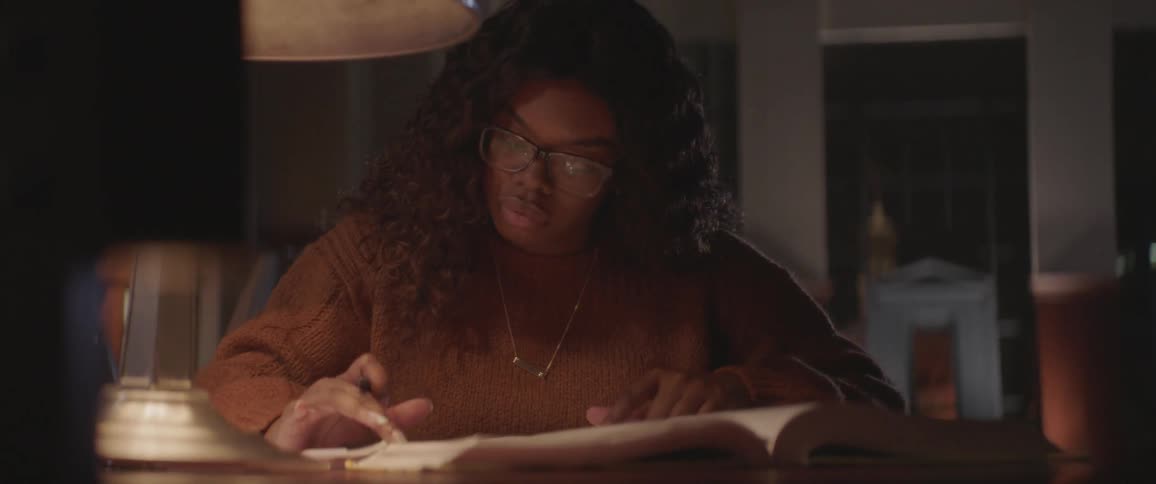 A woman is working at a desk at night with a book and calculator