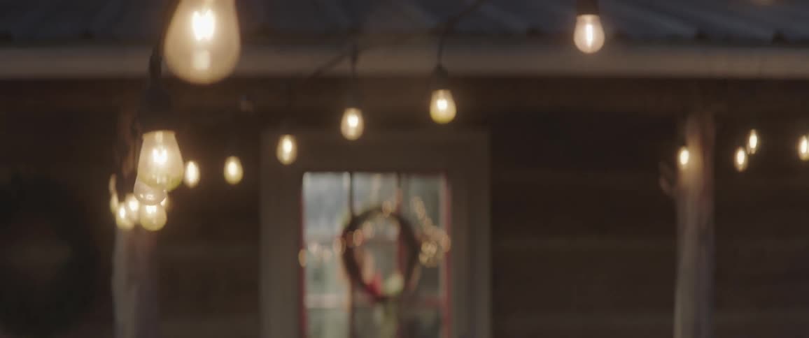 A wreath hangs on a door of a home that is lit up with lights