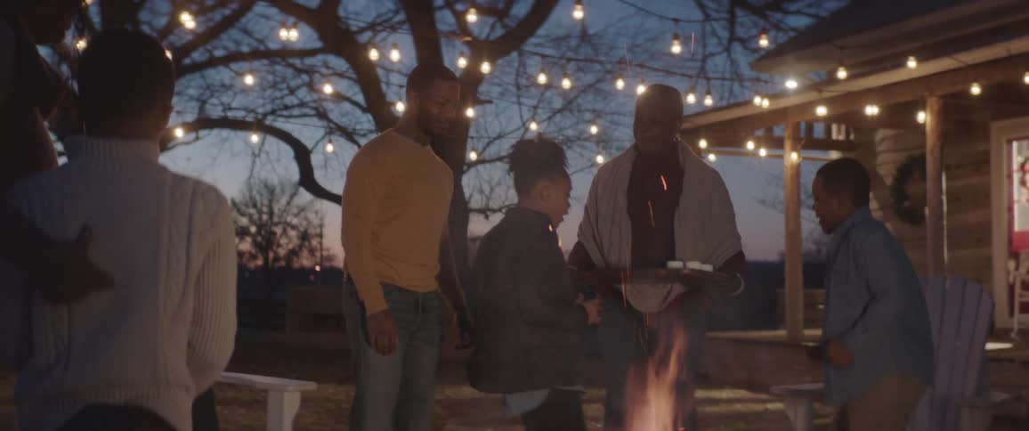 A family is gathered around a bonfire near a house