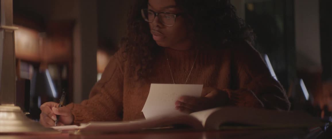 Black curly hair woman sitting at the table studies and writes down in the library at night