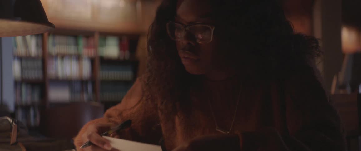 A woman looks at note cards sitting in a dark library