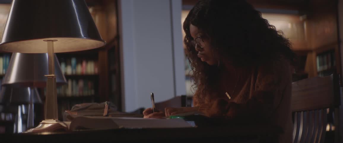 Black curly hair woman sitting at the table studies and writes down in the library