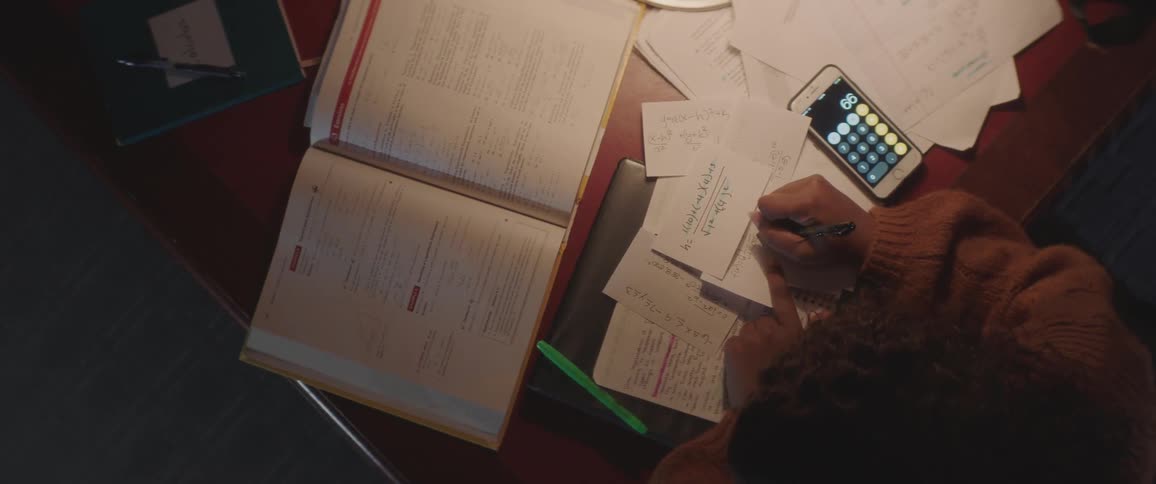 Person reading book and taking notes on desk at night