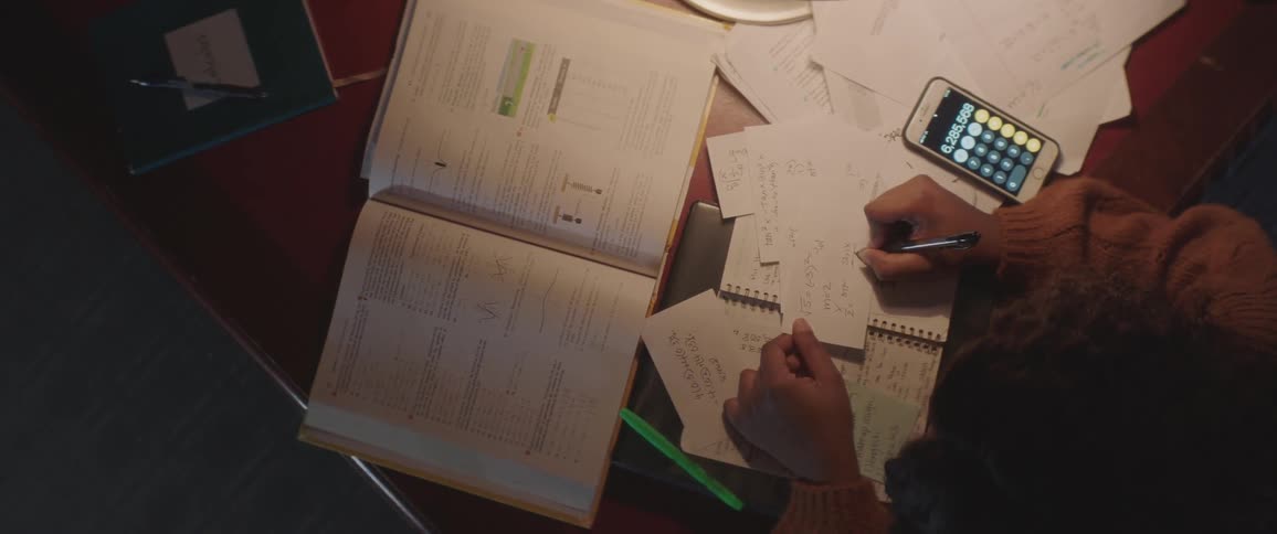 Woman perform calculations at table in dark room under overhead light