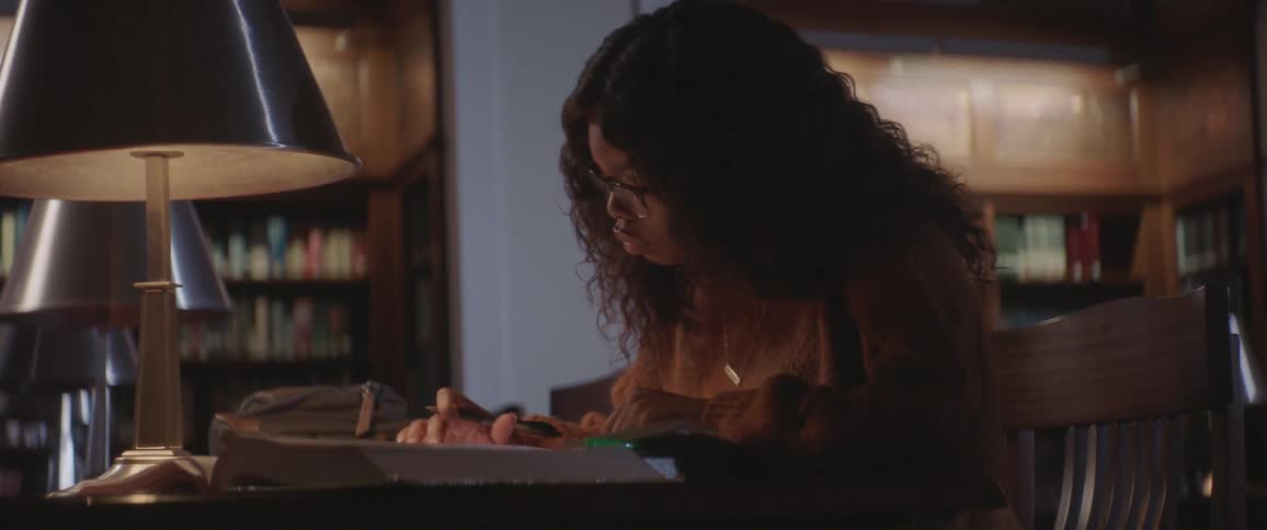 A woman is writing and punching in numbers at a library desk at night