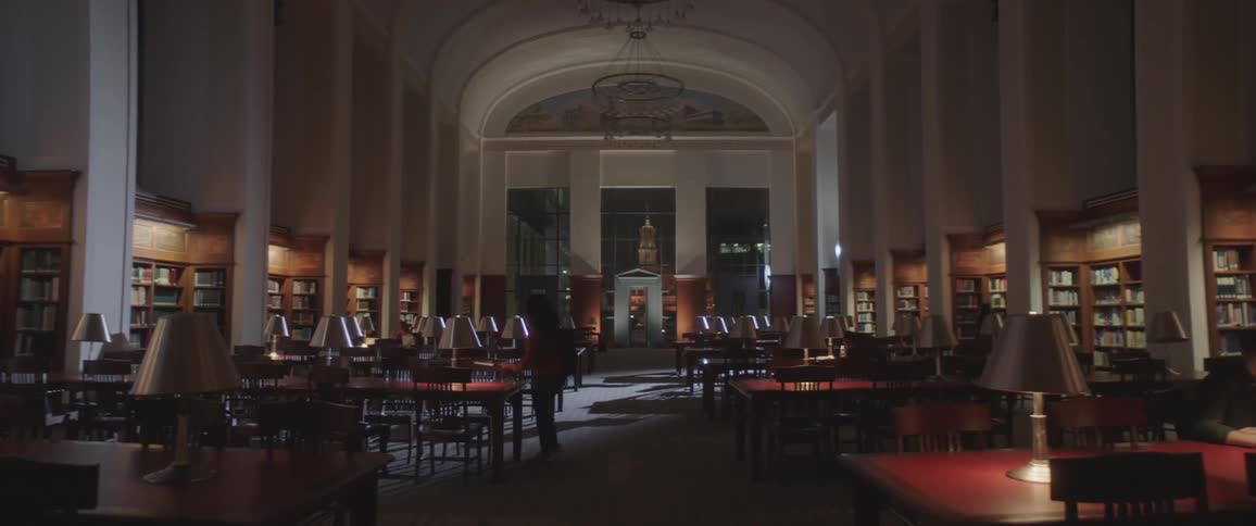 A person walks in the library and sits down