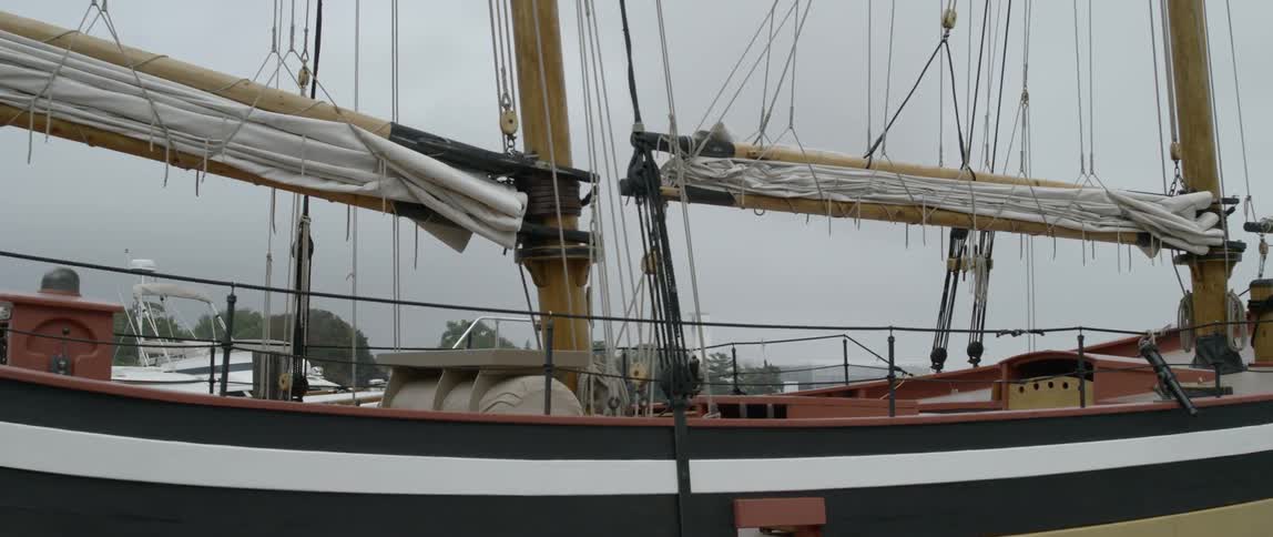 An old sail boat with two masts is docked on an overcast day