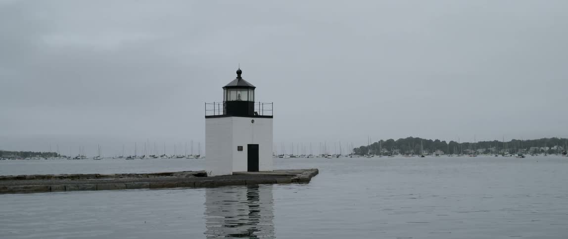 Lighthouse sits on low lying promontory with island and marina on horizon