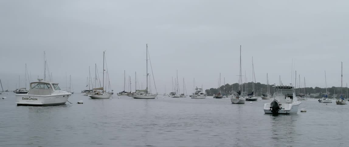 Many boats waiting off the coast of a headland on a cloudy day