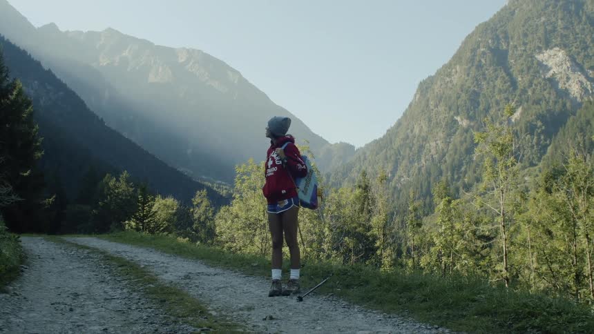 A black woman stands on a country road that cuts through a forest on a mountain