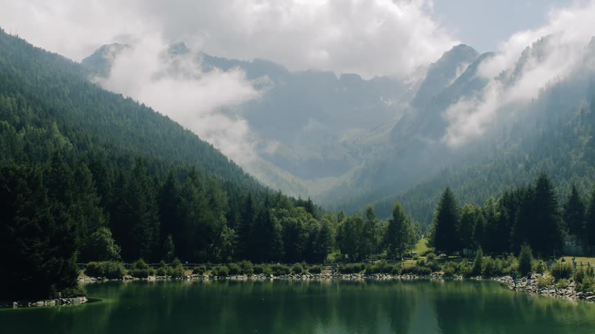A lake surrounded by tree covered mountains with low clouds and fog
