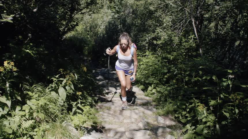 A woman hikes up a rocky trail between trees in a forest