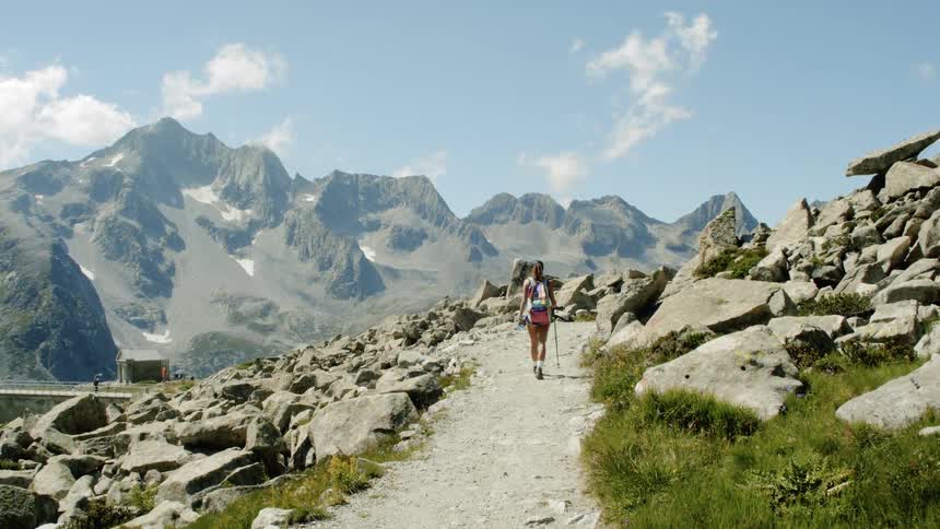 A person walking along a dirt path between large rocks along a mountain