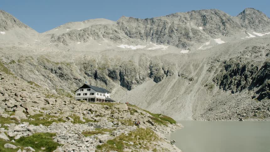 A building sits on a slope above the lake near the mountains