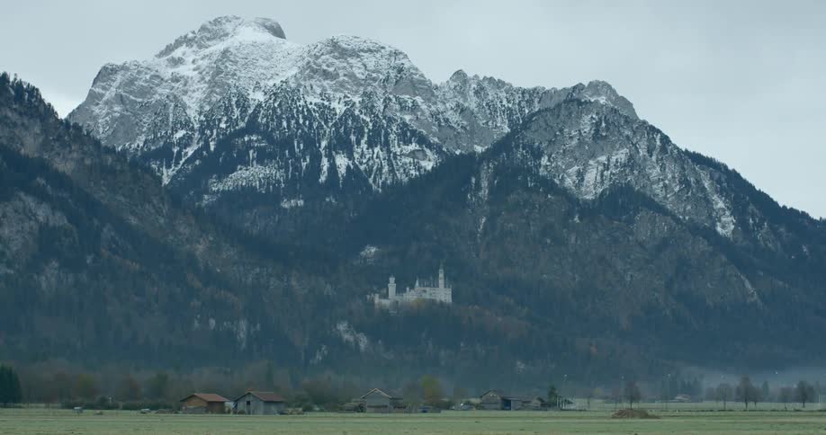 A homestead on grasslands lies before a large snow capped mountain