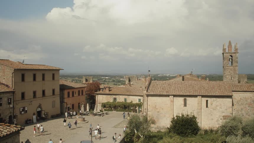 Pedestrians walk along courtyard near church with bell tower