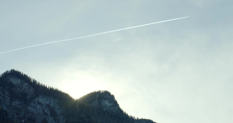 A plane shoots across a sky with mountains at dawn