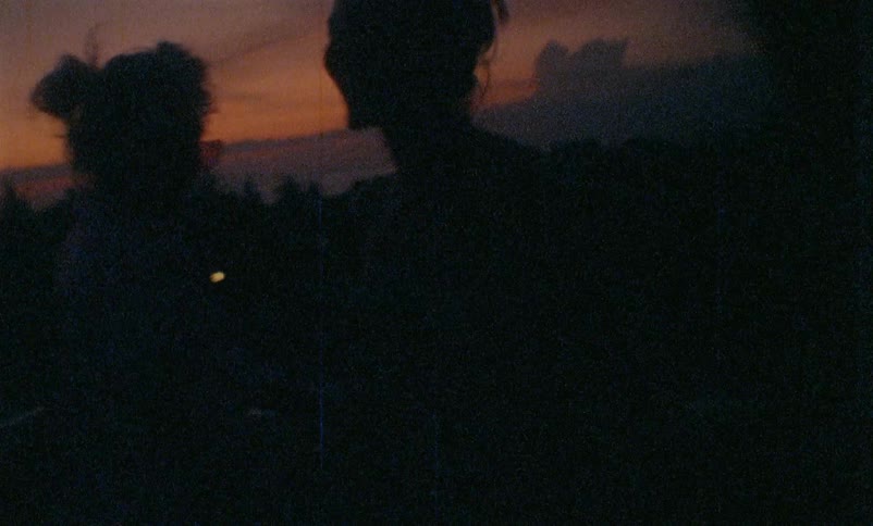 The silhouettes of two young women can be see as they playfully dance next to each other as the sun has just set in the sky behind them