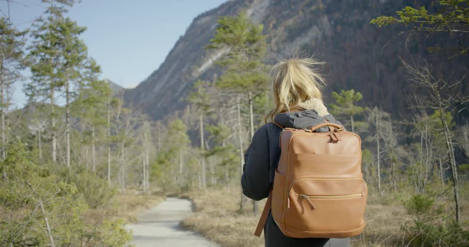 A woman walks on a wooded pathway trail beside a mountain