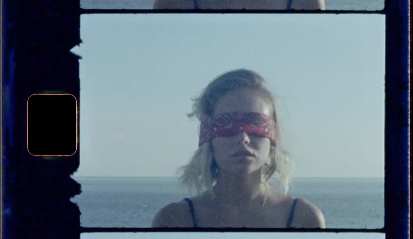 A blonde female stands by the coast blindfolded
