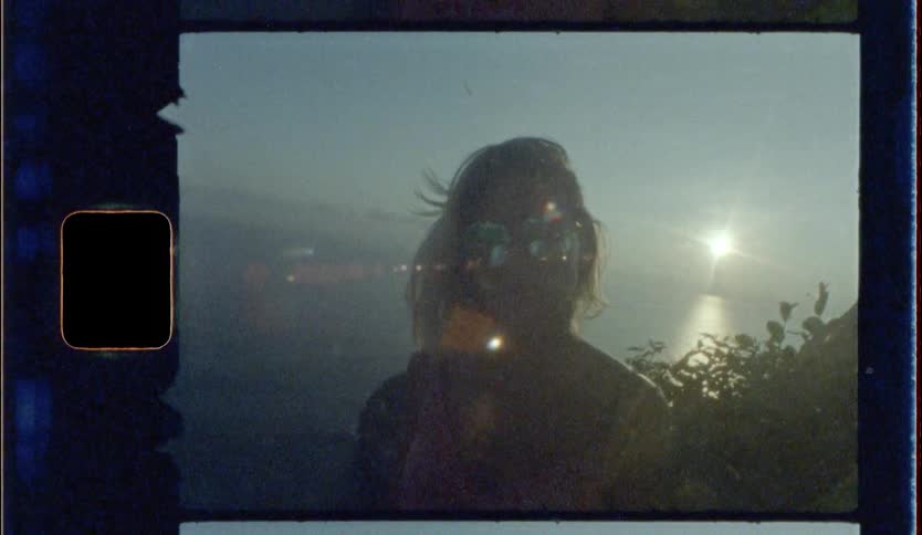 Blonde woman wearing sunglasses looks at the camera on a mountain while the sun goes down