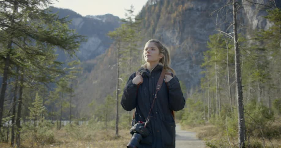 A woman with a camera walking in a pathway in the woods