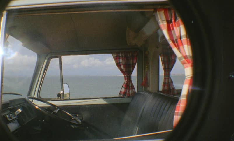 A vehicle with curtains parked near the ocean