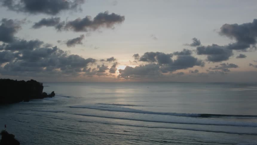 Calm waves roll into a tree lined cove at sunset