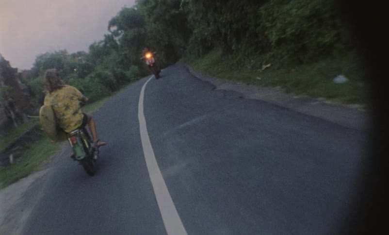 A person on a motor bike drives past two other people riding motor bikes in the opposite direction on a twolane highway