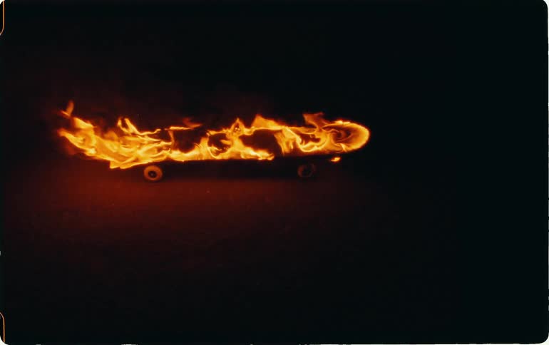 A skateboard is on the ground as it is engulfed in flames in a very dark setting