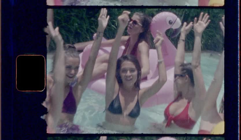 A group of attractive girls in bikinis splash and dance around in a pool